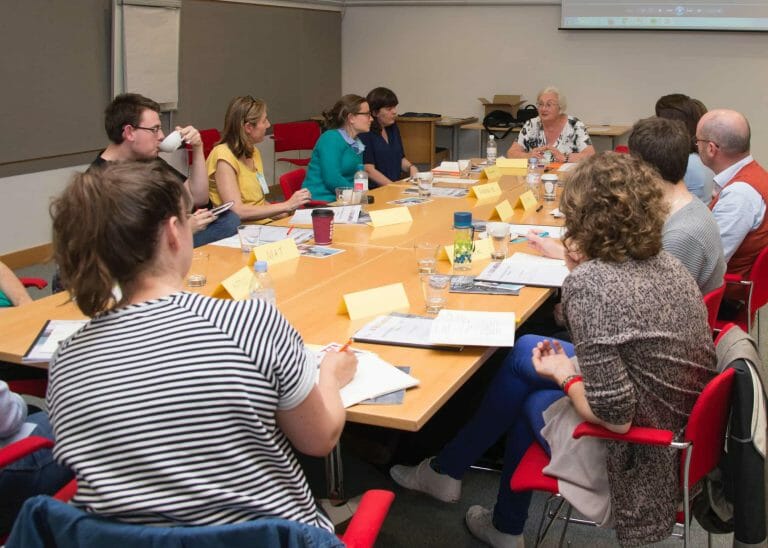 A group of people sit around a table with papers and name cards in front of them