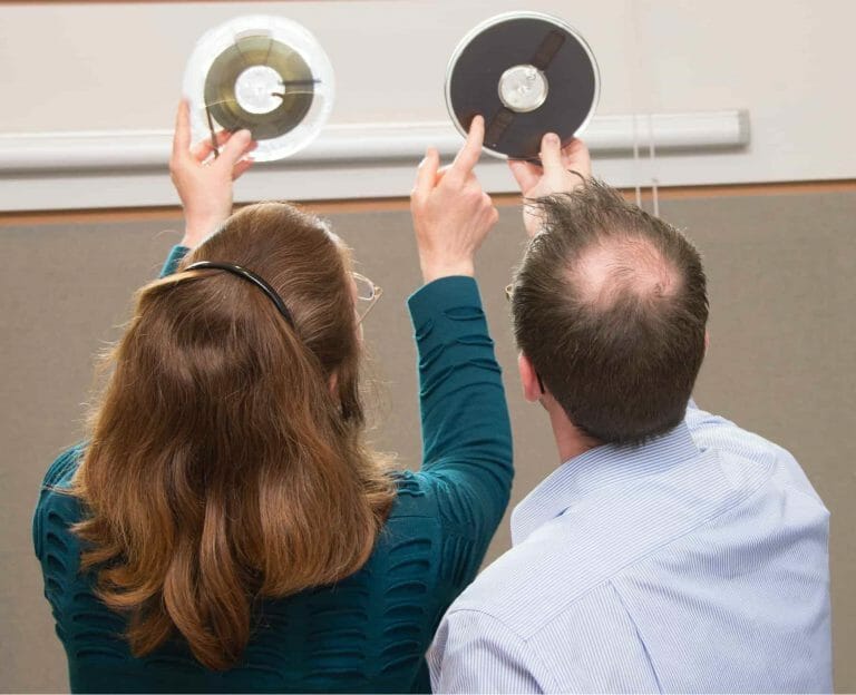 Two people hold up tape reels to the light