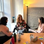 Three people sit talking around a table