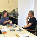Two people sit talking at a table