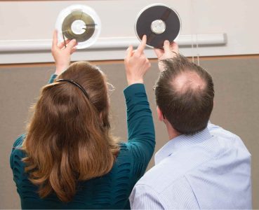 Two people hold up tape reels to the light
